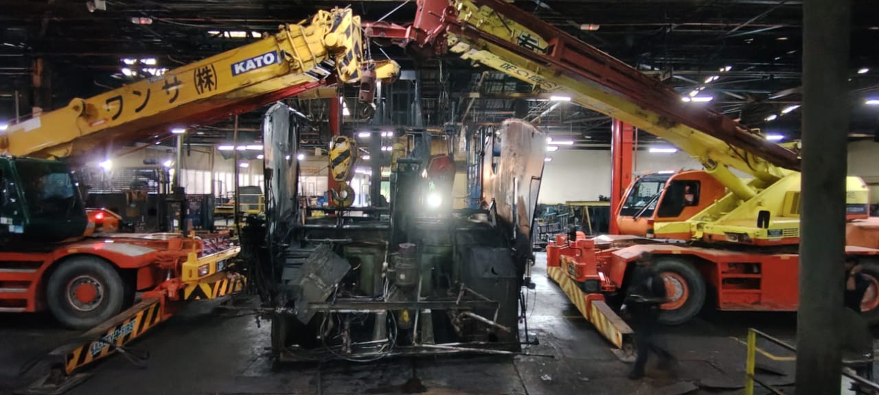 Two mobile cranes handling a large machine inside an industrial facility