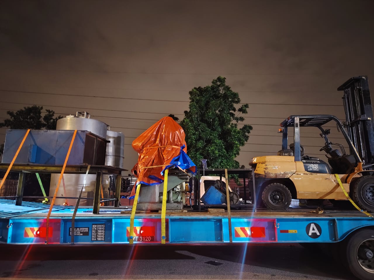 Machinery and a forklift strapped to a low loader trailer at night